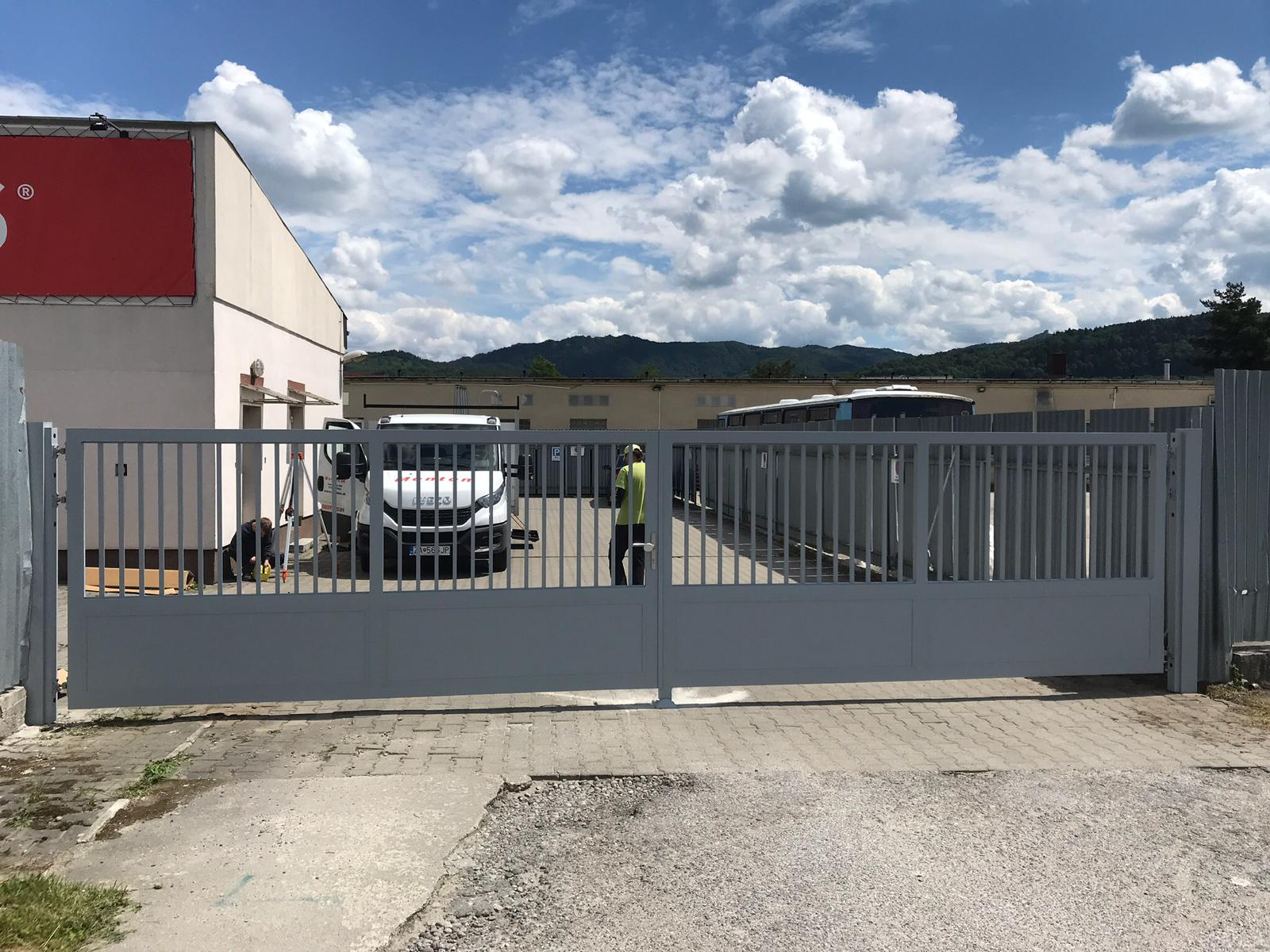 Šedá posuvná brána s bránkou pri firemnom areáli